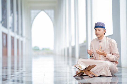  An Asian Muslim man is sitting and reading the Quran. The peace in the mosque makes it an energetic atmosphere of faith, with copy space.
