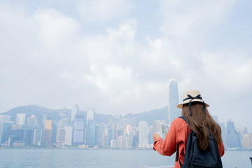 Asian tourist, cute woman with long hair are traveling in Hong Kong along with map and her camera with fun on her holiday,traveler relaxing and enjoying at Victoria harbour in Hong Kong.