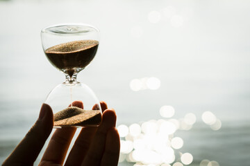 Hand holding the hour glass with bokeh of sea background. time to relax and summer concepts.