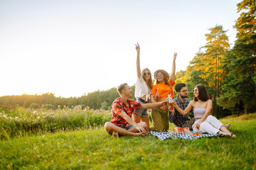 Group of young people gathered in garden for picnic. Friends have fun and  drink beer. Vacation,...