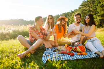 Group of young people gathered in garden for picnic. Friends have fun and  drink beer. Vacation,...