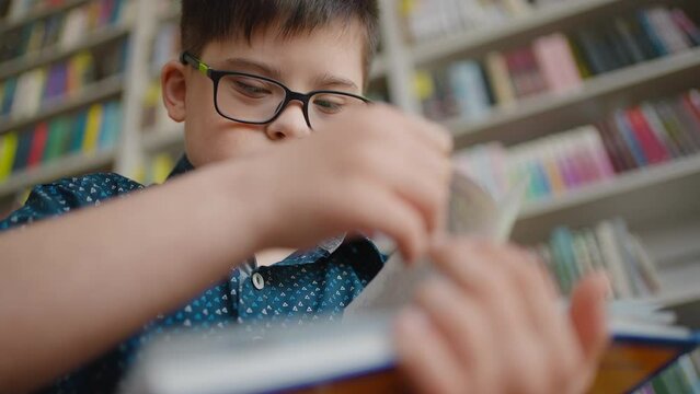 View from the bottom. Close-up of a child boy with Down syndrome, reading book in the school library