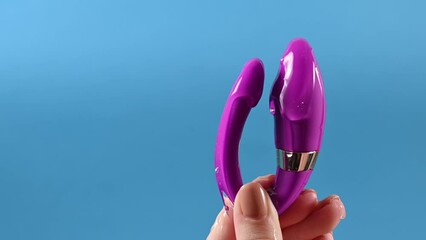 A woman holds a curved sex toy in lubrication on a blue background. Vaginally clitoral vibrator.