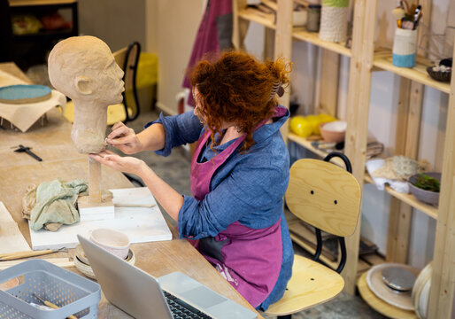 Female sculptor working in pottery studio workshop sculpting human head.