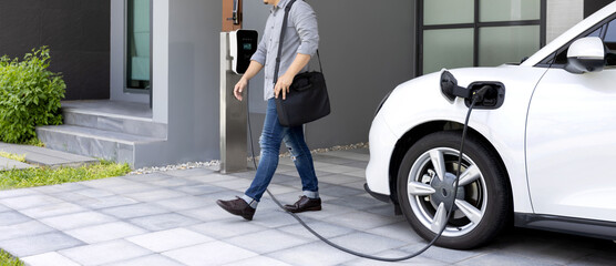 Progressive asian man and electric car with home charging station. Concept of the use of electric...