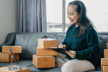 adult woman start up small business owner writing address on cardboard box at workplace.small business entrepreneur SME or freelance, female working with box at home.