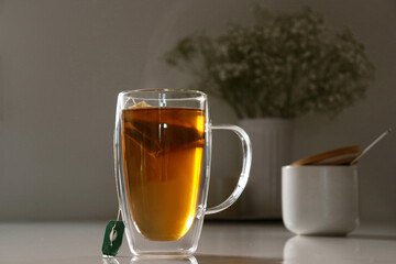 black tea in a glas cup on white table, flower in background with copy space