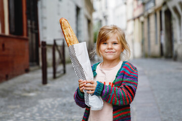 Adorable little preschool girl with fresh French baguette on the street side of the city. Happy...