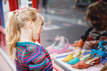 Little Girl looks at the window near the shopping center. Adorable happy child looking on shoes in store window.
