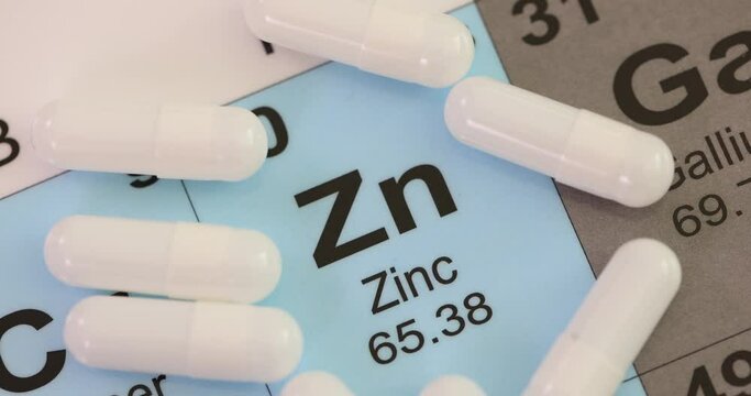 White capsules of zinc microelement lying on cardboard with chemical elements names. Concept of vitamins supplement for improving human health and treatment