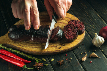 The chef cuts blood sausage on a kitchen cutting board with a knife. Cooking a national dish with...