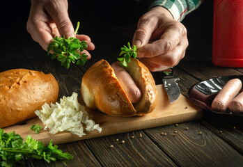 The cook prepares a hot dog on the kitchen table. The chef's hands add fragrant parsley to the hot dog. Street food idea with milk sausage and bun