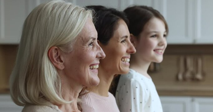 Portrait of three generational women family posing indoors, focus on mature happy blonde female turn her head and looking at camera. Lifetime from childhood to retirement, generations and motherhood