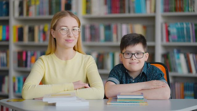 Portrait of a teacher and her primary school student boy with Down syndrome looking at camera
