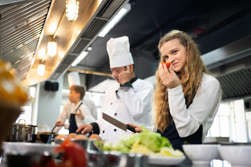 Portrait of a female student chef holding tomatoes in the kitchen.
