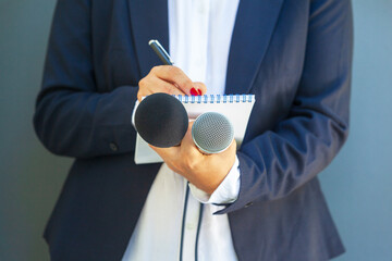 Journalist at media event or news conference, holding microphone, writing notes. Broadcast...