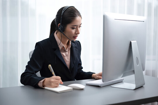 Asian call center with headset and microphone working on her laptop. Female operator provide exceptional customer service. Supportive call center agent helping customer on inquiry. Enthusiastic