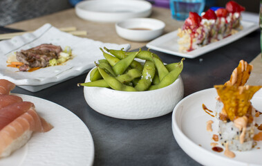 A table full of plates of food including sushi, green beans, and a bowl of rice.