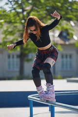 Cool young female grinding on a rail with aggressive inline skates. Tattooed chick skating in a...