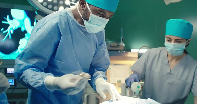 African American doctor performs surgical operation in modern hospital. Teamwork of professional medical surgeons in operating room. Concept of helth care and medical treatment.