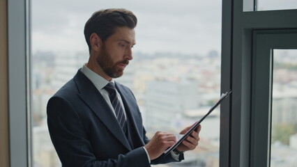 Businessman checking corporate papers standing at office window close up.