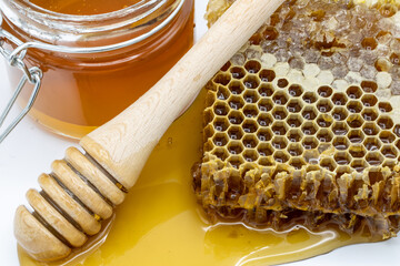 Closeup of jar of honey next to honeycomb and honey stick