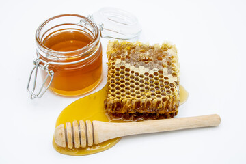 jar of honey next to honeycomb and honey dipper isolated on white background