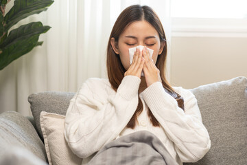 Sick, coronavirus or covid-19, attractive asian young woman, girl have a fever, flu and hand in use tissues paper sneezing nose, runny while sitting on sofa, couch at home. Health care on virus person