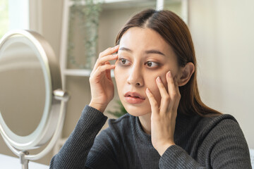Bored, insomnia asian young woman, girl looking at mirror hand touching under eyes with problem of black circles or panda puffy, swollen and wrinkle on face. Sleepless, sleepy healthcare person.