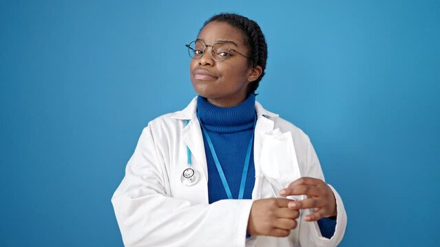 African american woman doctor standing wearing medical mask over isolated blue background
