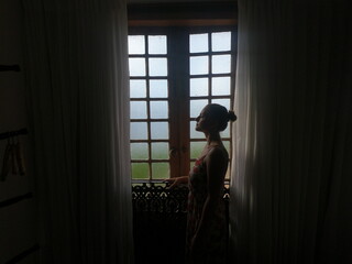 Silhueta de mulher em frente à janela com cortinas 