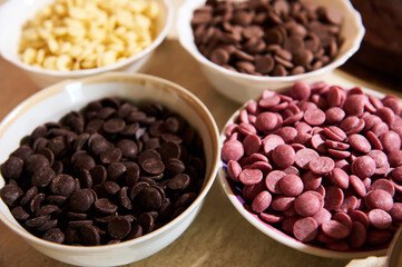 Fototapeta premium Dark, milk, white and ruby pink chocolate chips in bowls on marble kitchen countertop background. Food background. Still life