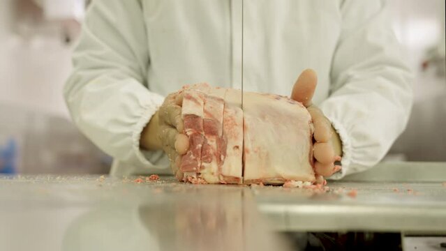 Close up. Hands of butcher using meat band saw  to slice meat cuts at meatpacking factory.