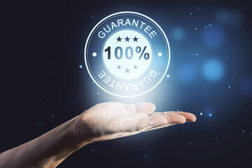 Close up of male hand holding glowing 100% guarantee stamp hologram on dark background with bokeh...