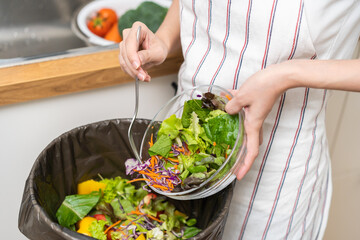 Compost from leftover food asian young housekeeper woman, female hand holding salad bowl use fork scraping waste, rotten vegetable throwing away into garbage, trash or bin. Environmentally responsible