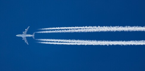 White aircraft at a distance and contrails in clear blue sky
