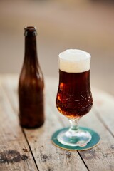 Vertical shot of a Dark beer cup and the bottle on table