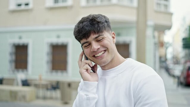 Young hispanic man talking on smartphone smiling at street
