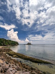 Vertical shot of a rocky beach under a cloudy blue sky