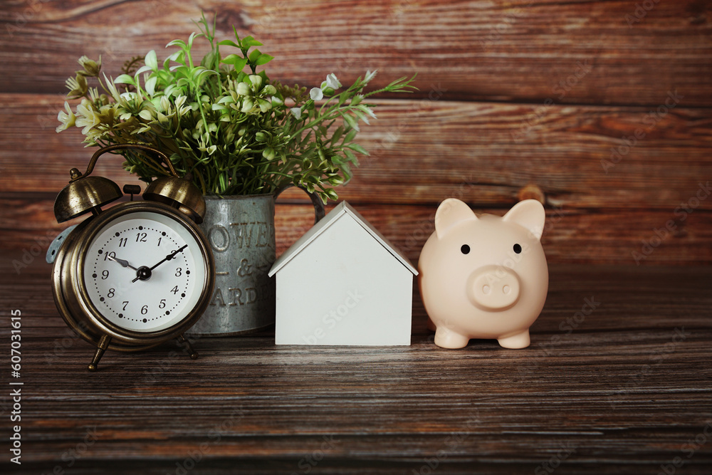 Poster house model with piggy saving and alarm clock on wooden background