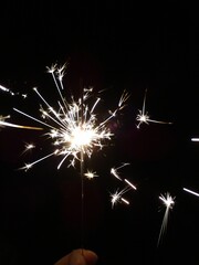 Vertical shot of a sparkler in a lady's hand sparkling at night
