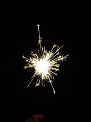 Vertical shot of a sparkler in a lady's hand sparkling at night