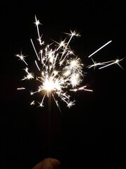 Fototapeta premium Vertical shot of a sparkler in a lady's hand sparkling at night