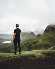 Man standing on a hill with mountains and a small lake in the background on a cloudy day