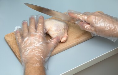 Closeup of human hand wearing disposable plastic gloves and cutting meat on board