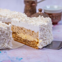 Closeup of the piece of coconut cheesecake covered with grated coconut with a blurry background