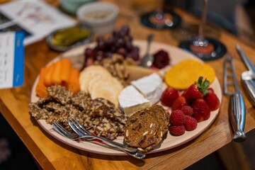 Closeup shot of a cheese plate with brie cheese, berries, crackers, etc., on the table