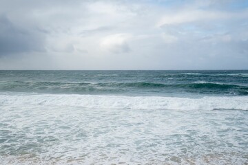 Beautiful scenery of beach with waves under a cloudy sky - great for wallpapers