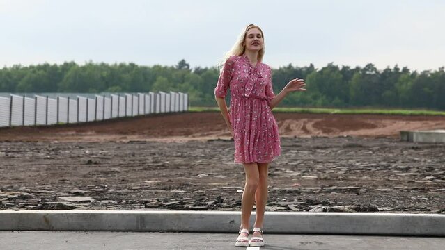 Young beautiful blonde girl in a summer dress dances on a construction site
