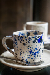 White coffee cup with blue spots on a saucer with a spoon on a wooden table